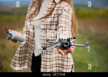 Close up of woman holding flying drone toward camera with spinning propellers and controller in hand, shallow depth of field, concept of modern technology and hobby Stock Photo