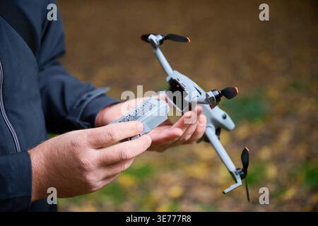 Man replaces battery in drone before flight. Close up of hands installing battery into quadcopter in park, preparing equipment for use, concept of modern technology and maintenance Stock Photo