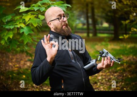 Man gestures OK sign while holding drone and controller. Bearded man satisfied with setup in park, expressing approval and confidence, concept of success, ease of use and technology Stock Photo