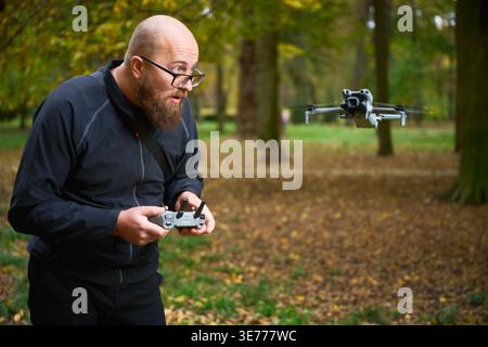 Man controlling flying drone. Bearded man operating quadcopter in park, focused on flight and reacting with excitement, concept of modern technology and hobby Stock Photo