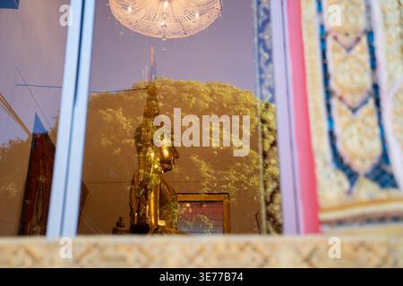 A golden Buddha statue appears behind temple glass with tree reflections. A chandelier hangs above the calm interior view. Stock Photo