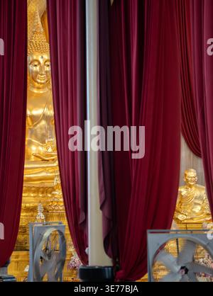 A golden Buddha statue appears between deep red curtains inside the temple. Draped fabric frames the shrine view. Stock Photo