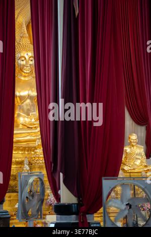 A golden Buddha statue appears between deep red curtains inside the temple. Draped fabric frames the shrine view. Stock Photo