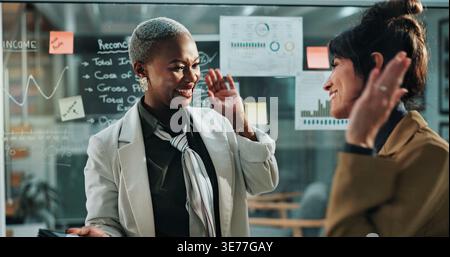 Happy women, night and teamwork with high five in office for business success or profit. Excited, female people or colleagues working late with smile Stock Photo