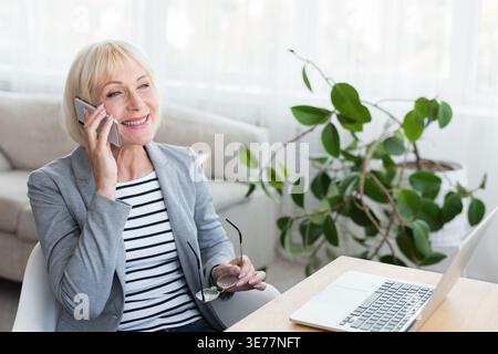 Elderly businesswoman talking on phone, consulting client Stock Photo