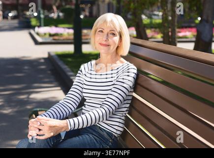 Senior woman relaxing on bench in city park Stock Photo