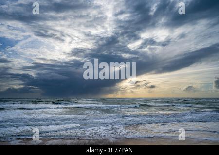Dramatic storm clouds loom over the choppy waves of the Atlantic Ocean in Cadiz. Light breaks through the horizon on the beach, capturing the raw powe Stock Photo