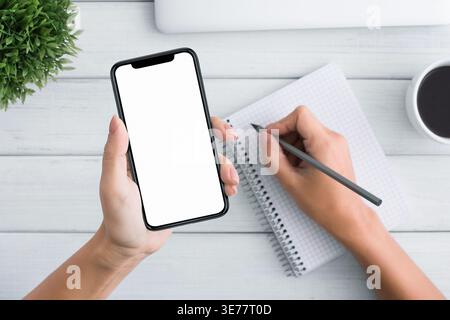 Woman hand holding blank smartphone and writing in notebook Stock Photo