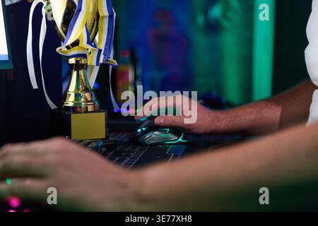 Gamer Hands Using Mouse Beside Trophy After Victory in Competitive Esports Tournament Setup Stock Photo