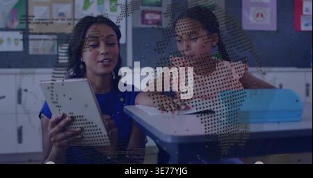 Holding tablet, teacher in blue guiding girl in pink ruffle shirt at blue desk with notebook Stock Photo