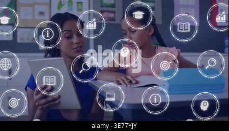 Holding tablet, woman in blue guiding girl in pink writing at classroom desk with notebook, icons Stock Photo