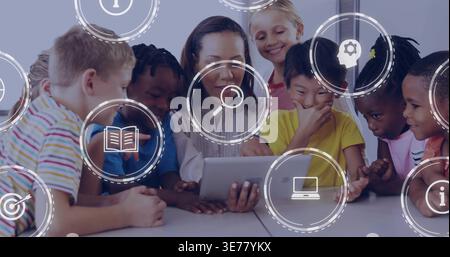 Diverse students with female teacher in classroom, tapping tablet, icons floating, bright clothes Stock Photo