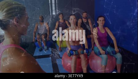 Leading instructor guiding group in workout gear on fitness balls in gym, with dumbbells overlay Stock Photo