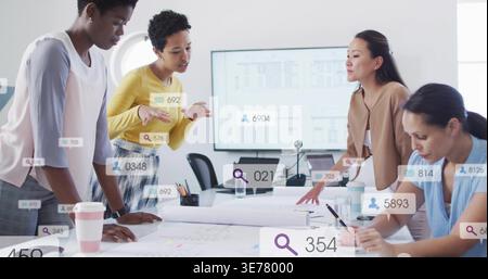 Reviewing four women studying blueprints in office, wearing business-casual attire, laptop visible Stock Photo