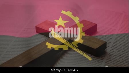 Lying wooden Christian cross casting soft shadow across open book on tabletop, Angola flag overlay Stock Photo