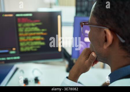 African American young adult man analyzing code on desktop monitor, working in software development or cybersecurity. Useful for IT services, programming, data security marketing Stock Photo