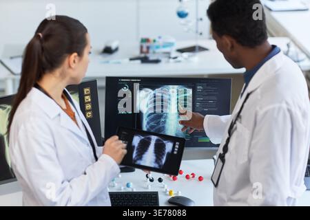 Multiethnic doctors reviewing chest x ray scans on monitor and tablet, discussing diagnosis in radiology lab. Ideal for healthcare technology, medical teamwork, diagnostic imaging Stock Photo