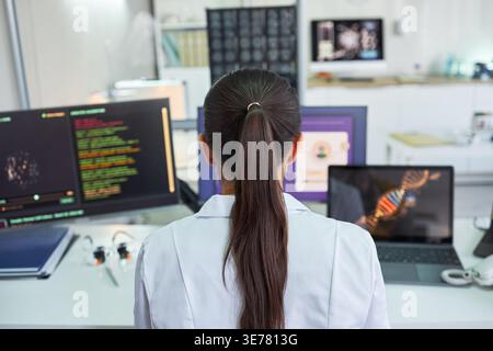 Rear view of young adult woman scientist analyzing genetic data across multiple screens in laboratory, supporting genomics research and biotech innovation marketing, wide shot Stock Photo