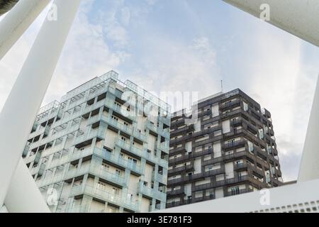 View of modern buildings with contrasting light blue and dark brown facades reach towards a soft, cloudy sky, framed by a white architectural structur Stock Photo