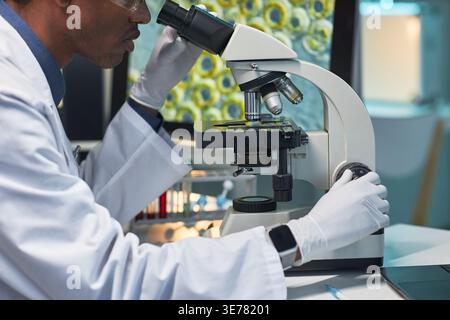 Close up of Black male scientist examining sample through microscope in laboratory, conducting medical research. Ideal for healthcare innovation, diagnostics, biotechnology marketing Stock Photo