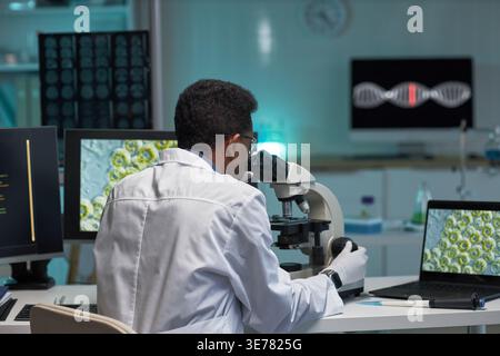 Black male scientist examining specimen through microscope in medical laboratory, analyzing research data for genetics study. Ideal for biotech innovation, healthcare research, diagnostics marketing Stock Photo