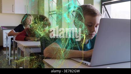 Working boy in teal shirt typing on silver laptop at classroom desk, green gold particle swirl Stock Photo