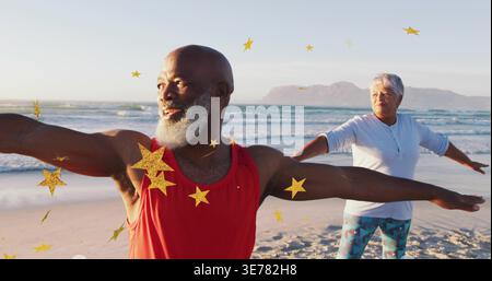 Stretching man in red tank top holding arms on sandy beach near ocean, golden confetti falling Stock Photo