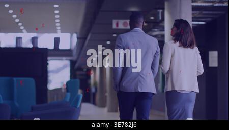 Walking two professionals wearing business attire moving down office corridor, with blue chairs Stock Photo