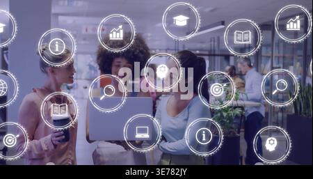 Gathering three colleagues leaning over silver laptop in open office, in light tops, with UI icons Stock Photo