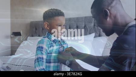 Smiling boy sitting on bed, man leaning fastening plaid shirt buttons, wristwatch, HUD graphics Stock Photo