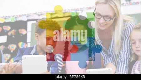 Leaning teacher in striped blouse guiding kids on white tablets in school, jigsaw overlay, board Stock Photo