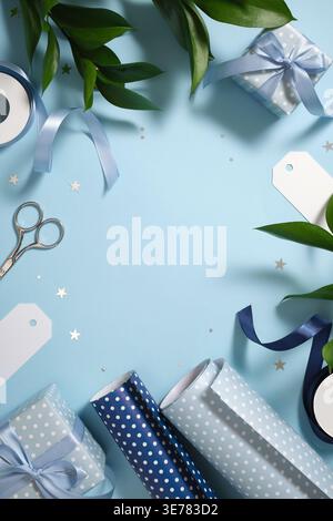Gift wrapping with blue wrapping paper, ribbon, scissors, and small gift boxes on blue backdrop. Copy space. Stock Photo