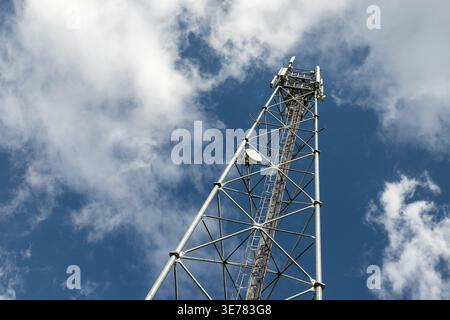 Bottom perspective pov of modern metal steel mobile 5g network wireless telecom tower against clear blue sky background on bright day. Microwave Stock Photo