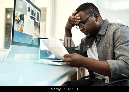 Computer screen, documents and stress with web designer black man in office for problem solving. Paperwork, pc and reading with African developer at Stock Photo