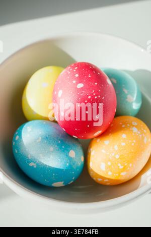 Five multicolored speckled Easter eggs in the bowl close up. Creative homemade natural eggs colored with synthetic dye and oil on white table under br Stock Photo