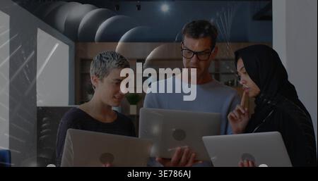 Examining three colleagues holding laptops in modern office, wearing light blue sweater and hijab Stock Photo
