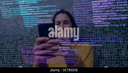 Holding smartphone, woman viewing screen against mosaic wall, wearing mustard sweater, showing code Stock Photo