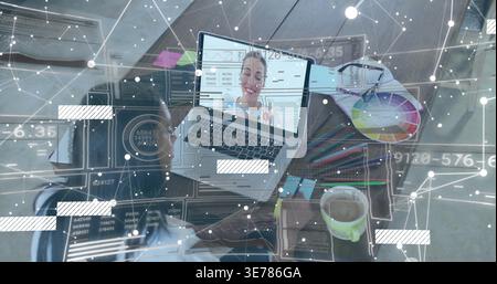 Working woman wearing casual jacket at home desk using laptop call, color wheel, pens, data overlay Stock Photo