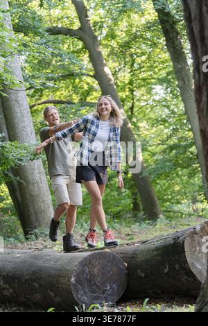 Young couple balancing on logs enjoying forest adventure together Stock Photo