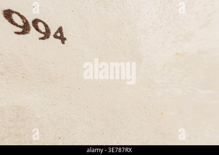 A detailed view of the numeral 994 imprinted on a rough, light-colored background with subtle speckles and variations in texture Stock Photo