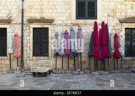 Row of colorful closed umbrellas against stone wall in Dubrovnik old town. Urban travel detail. Stock Photo