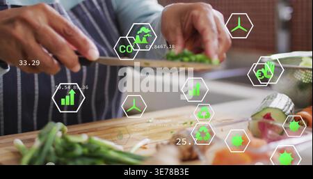 Knife starting cut, hands in apron are chopping herbs on board while overlays showing CO2 tracking Stock Photo