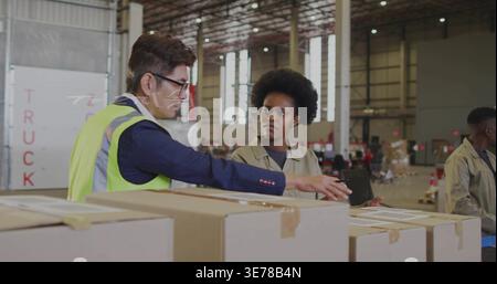 Pointing manager in vest and glasses explaining labels on stacked boxes by TRUCK door at warehouse Stock Photo
