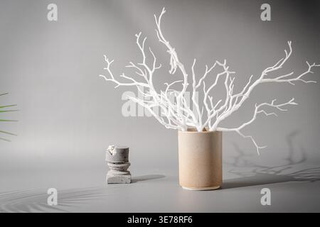 Minimalist composition with white plastic branches placed in ceramic vase against gray background Stock Photo
