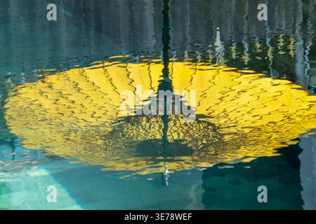 Yellow asian parasol umbrella reflection in the water of a swimming pool,  asian travel background Stock Photo