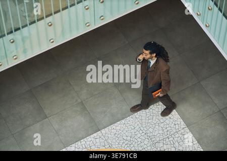 Businessman Walking and Talking on Phone in Office Lobby Stock Photo