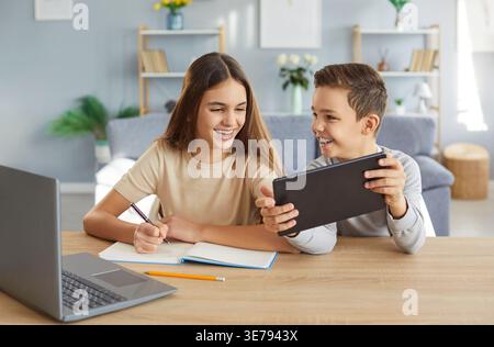 Two children are happily doing their homework and having fun using modern gadgets. Stock Photo
