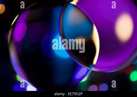Glass spheres refracting and reflecting vibrant purple, blue, and gold bokeh lights in a dark setting Stock Photo