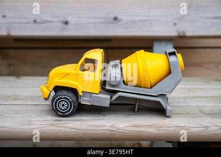 Yellow toy cement mixer truck on wooden bench with blurred rustic background Stock Photo