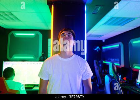 Young Gamer Standing Under Neon Lights in Modern Esports Gaming Room With Computers and Chairs Stock Photo